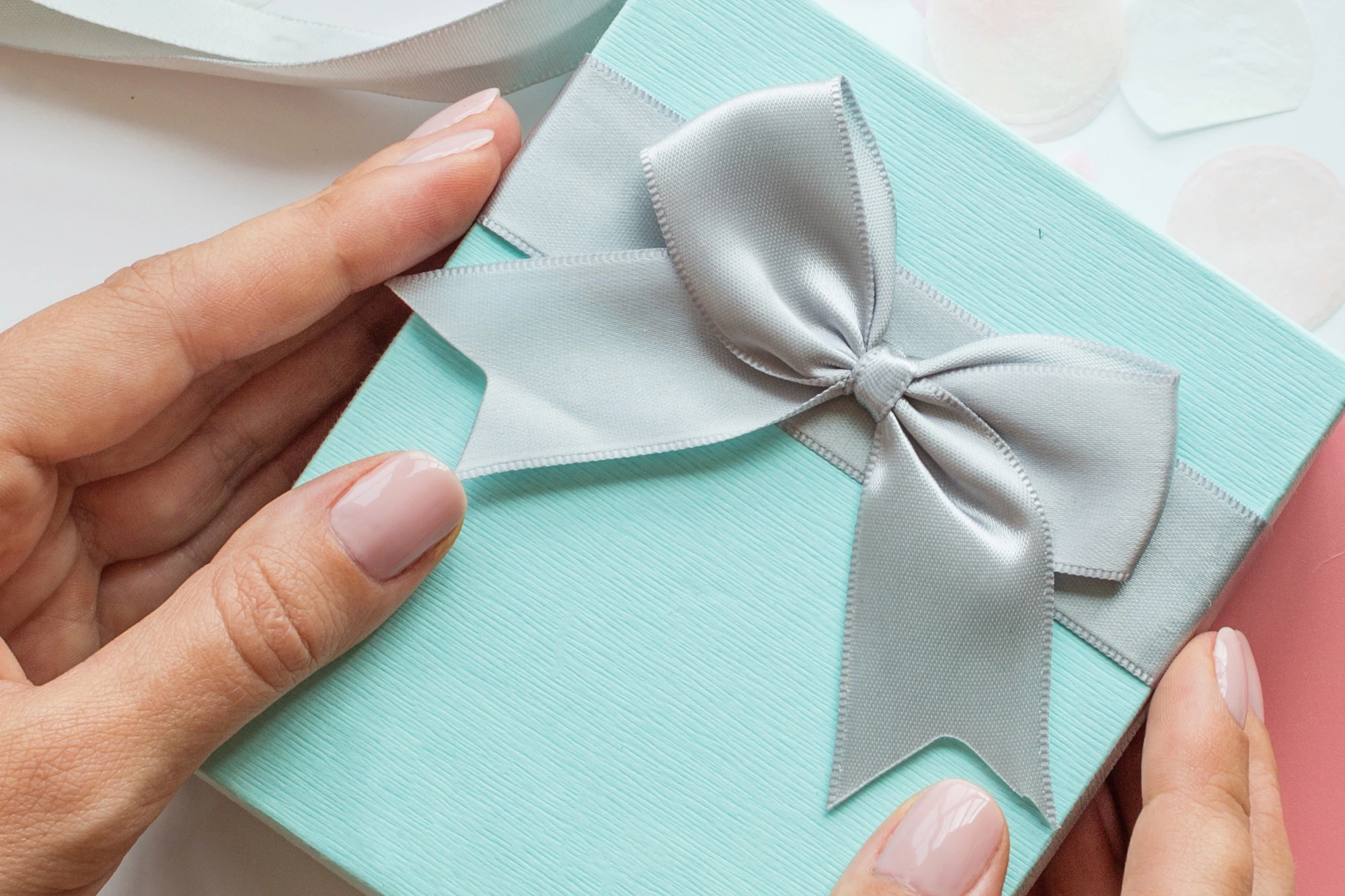 Hände halten ein türkisfarbenes Geschenk mit silberner Schleife