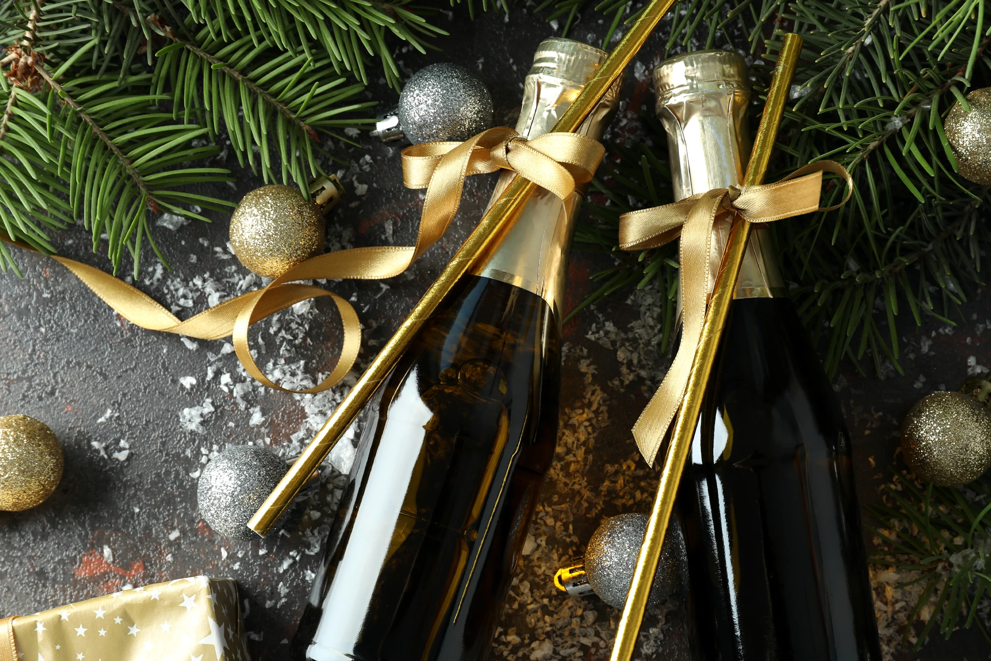 Dekorierte Champagnerflaschen mit goldenen Bändern zwischen Tannenzweigen und Weihnachtsdeko