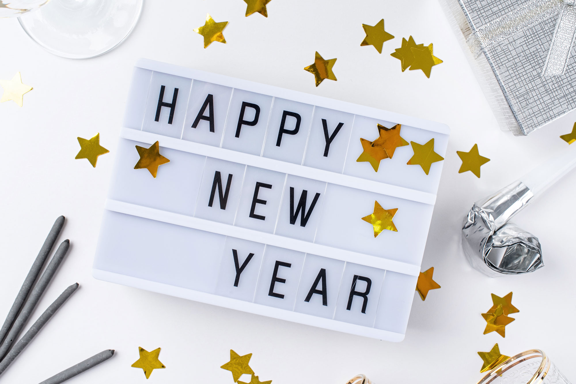 Leuchtbox mit Schriftzug „Happy New Year“ umgeben von goldenen Sternkonfetti und Partyaccessoires