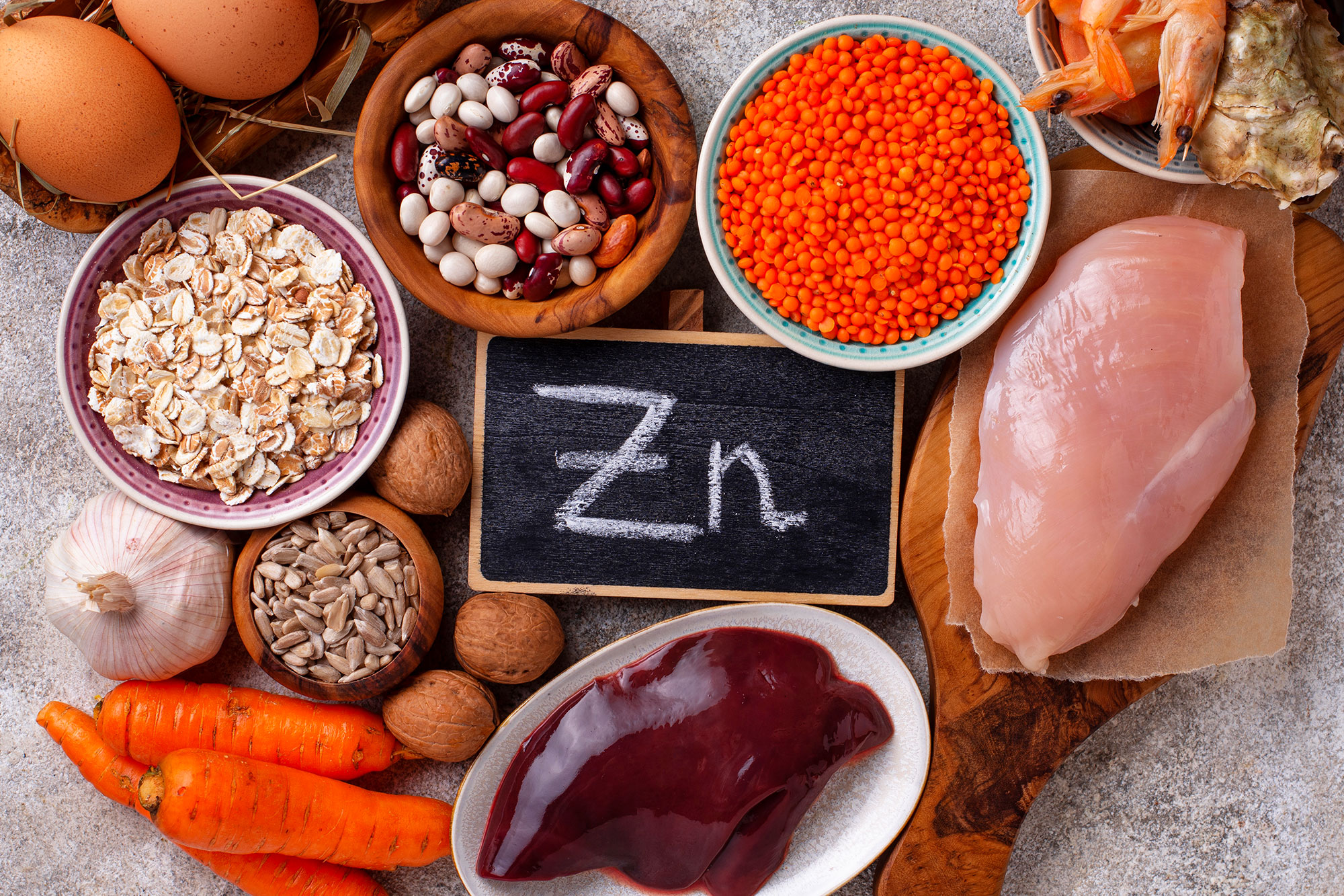 Verschiedene Lebensmittel wie Nüsse, Linsen, Fleisch und Eier umgeben eine Kreidetafel mit der Aufschrift „Zn“