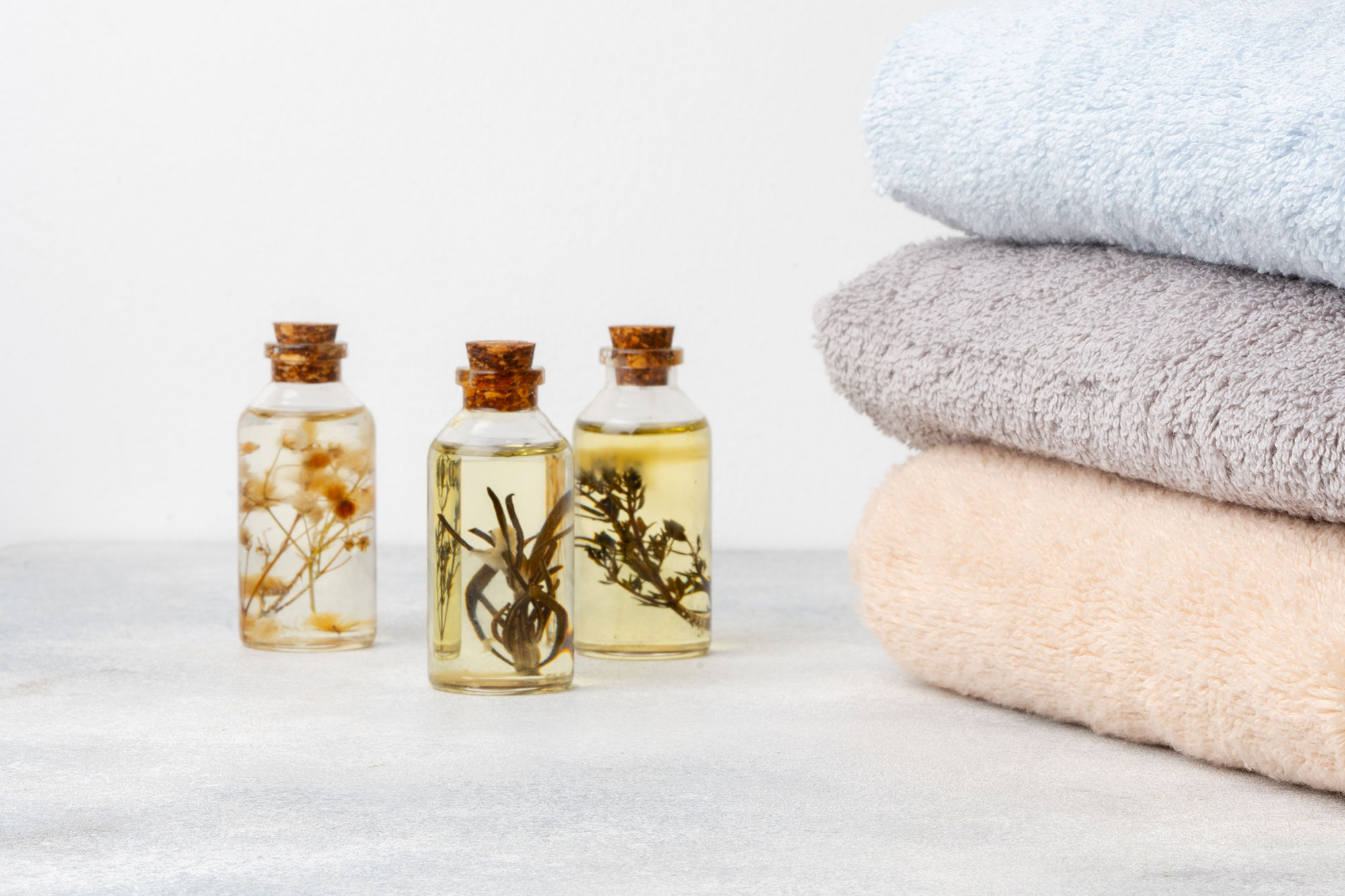 Kleine Fläschchen mit ätherischen Ölen neben gefalteten Handtüchern auf hellem Untergrund