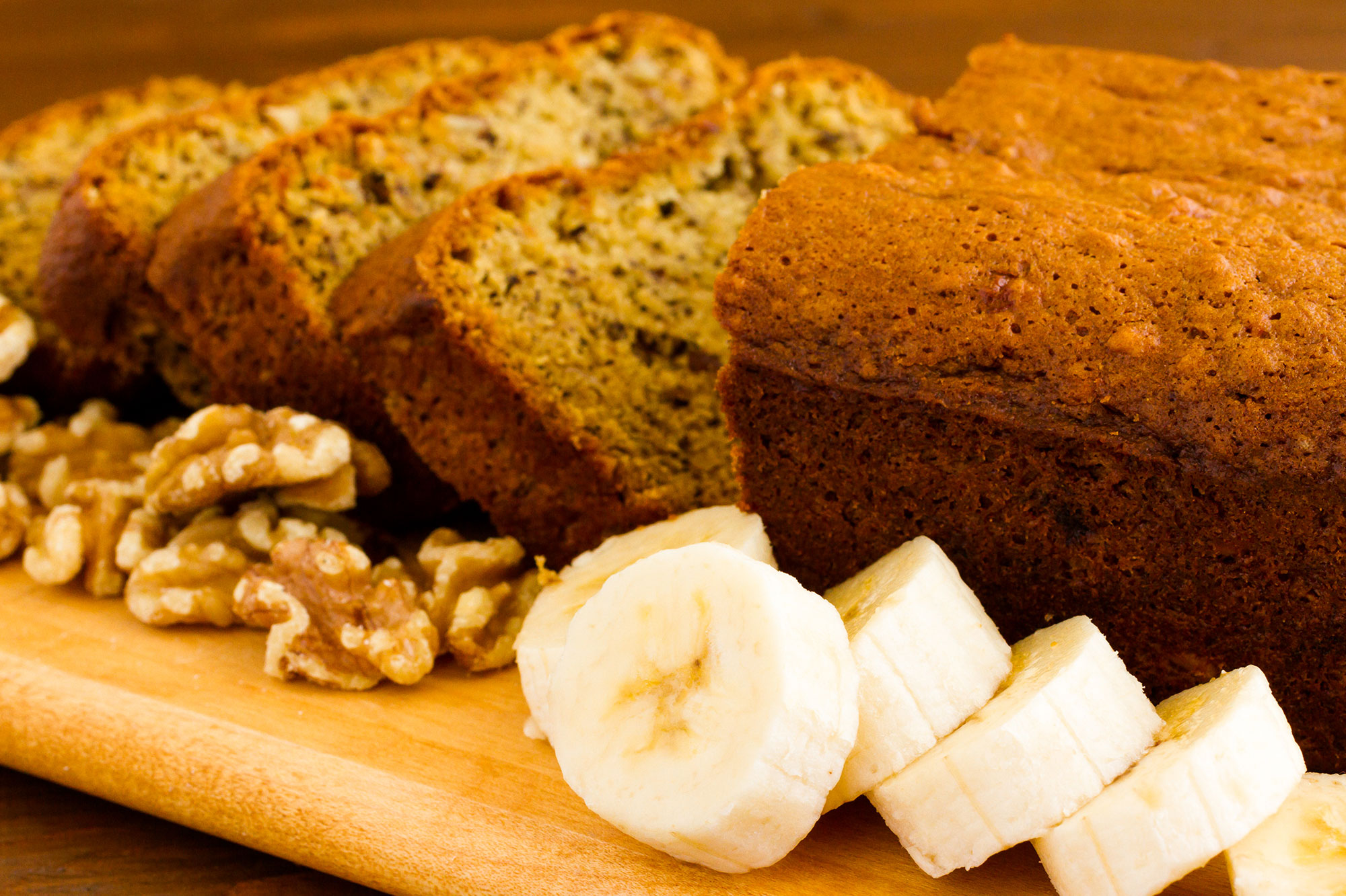 Geschnittenes Bananenbrot auf Holzbrett mit Walnüssen und Bananenscheiben dekoriert