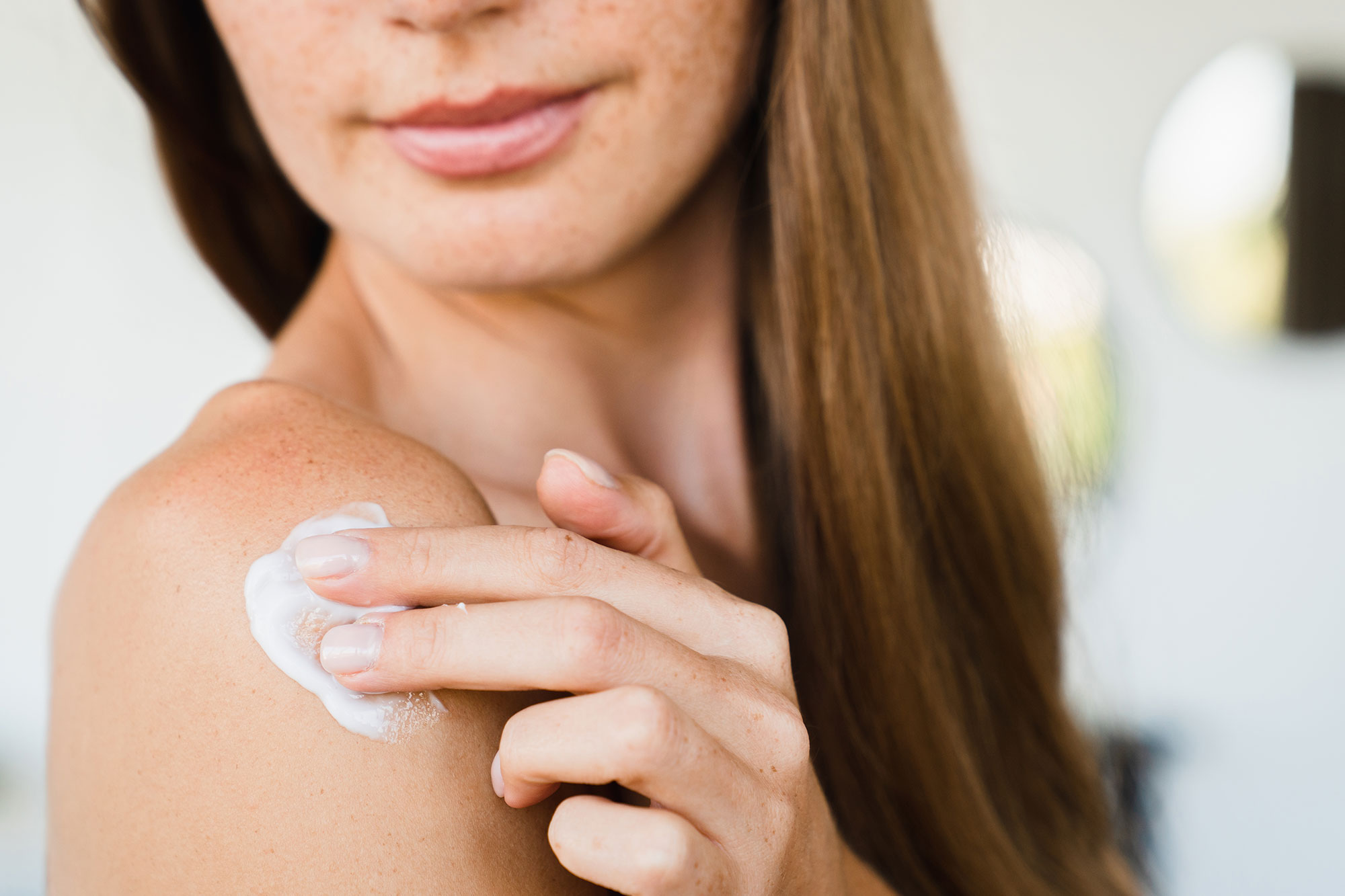 Frau trägt weiße Creme auf ihre Schulter auf