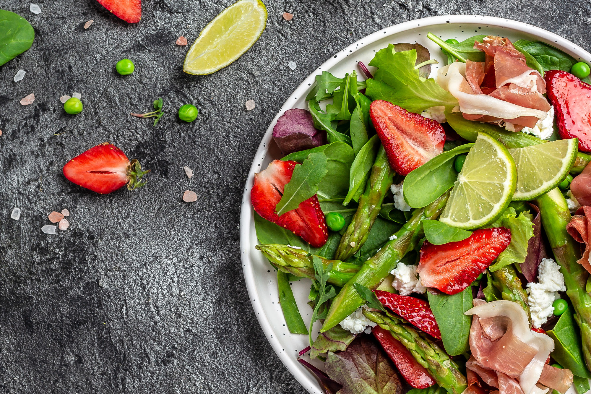 Schüssel mit gemischtem Salat aus Spinat, Erdbeeren, Limette und Nüssen auf dunklem Untergrund