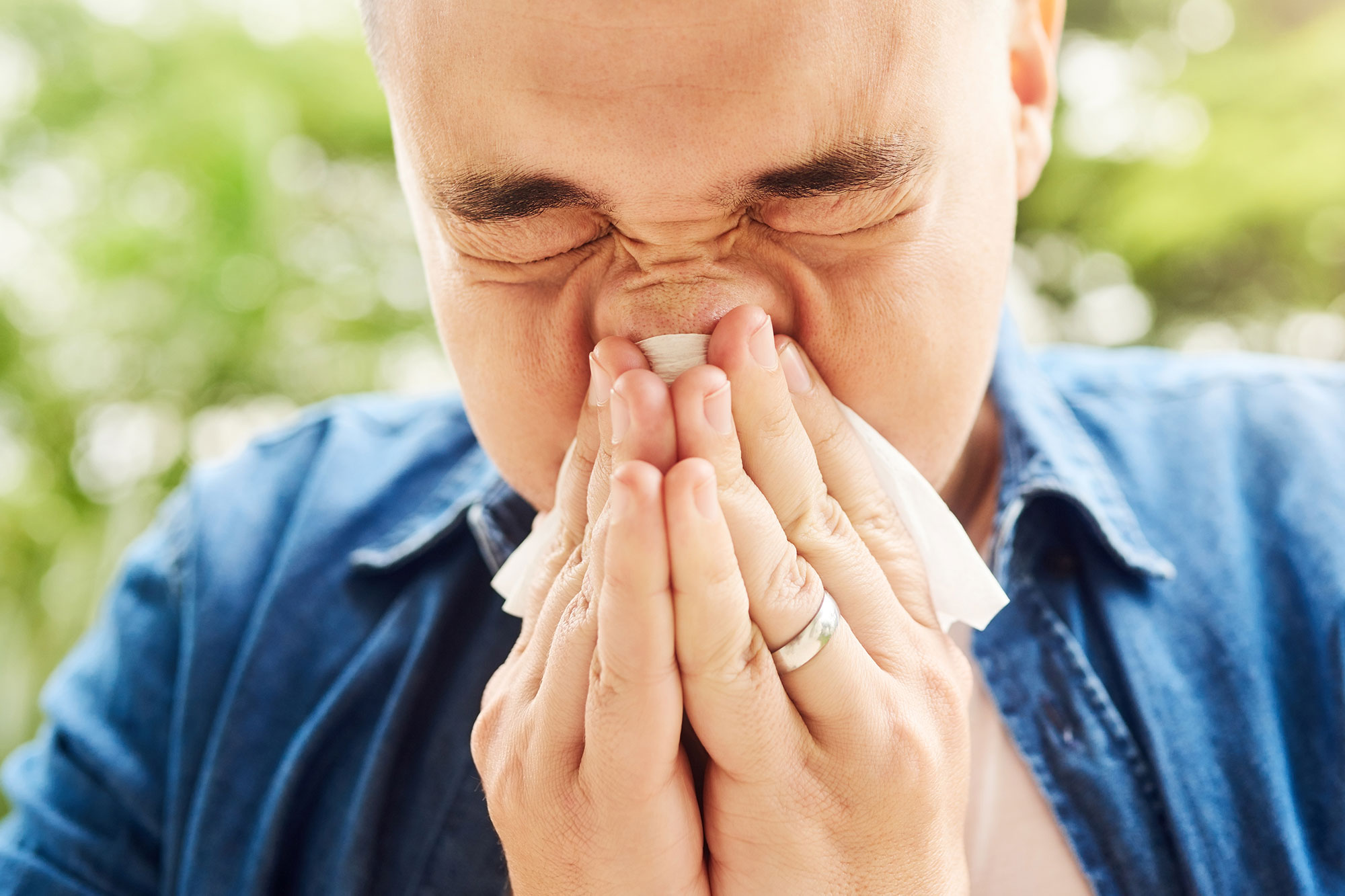 Mann niest in ein Taschentuch, Symbol für Pollenallergie und Heuschnupfen