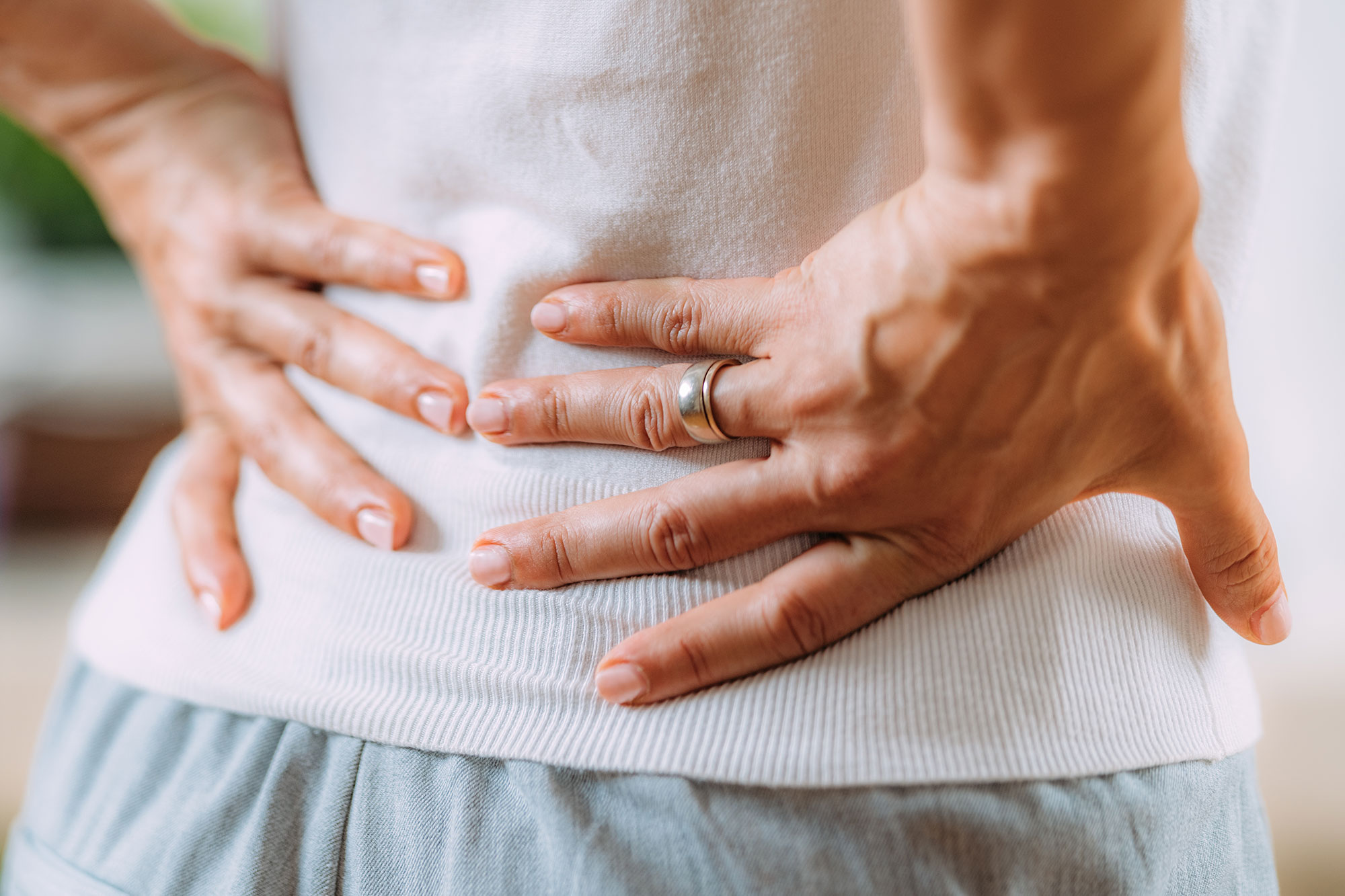 Person hält sich mit beiden Händen den unteren Rücken, Symbol für Rückenschmerzen