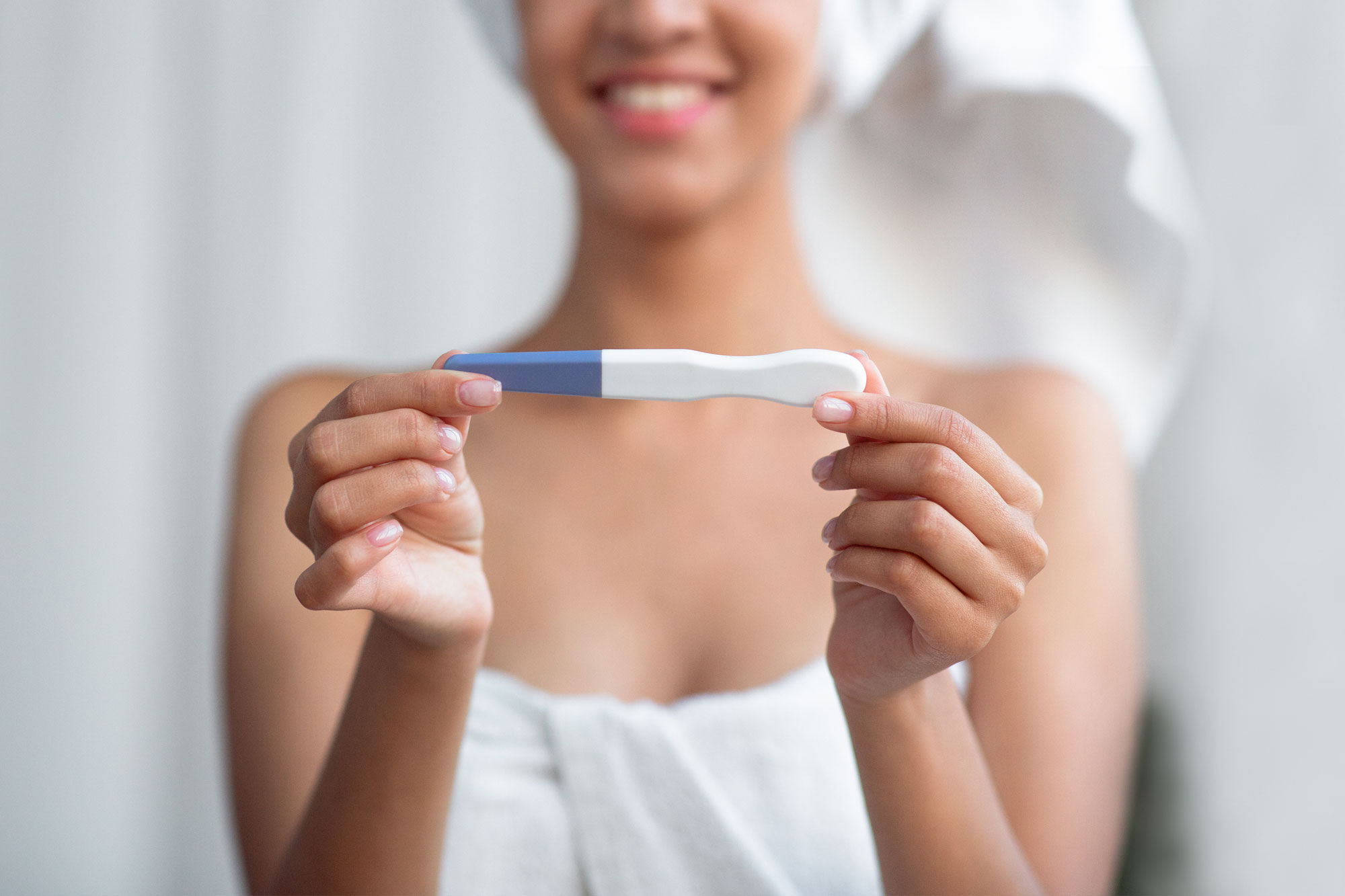 Lächelnde Frau hält einen positiven Schwangerschaftstest in den Händen