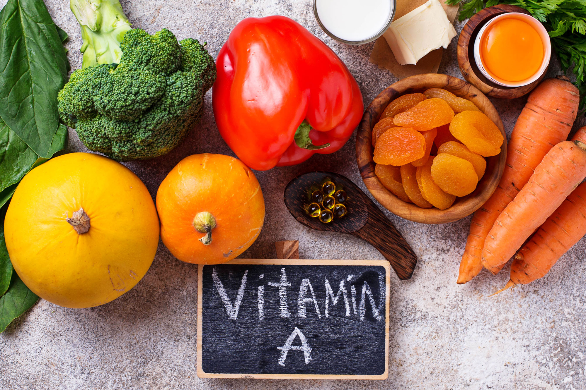 Verschiedene Lebensmittel wie Karotten, Paprika, Brokkoli und Aprikosen mit Tafel „Vitamin A“