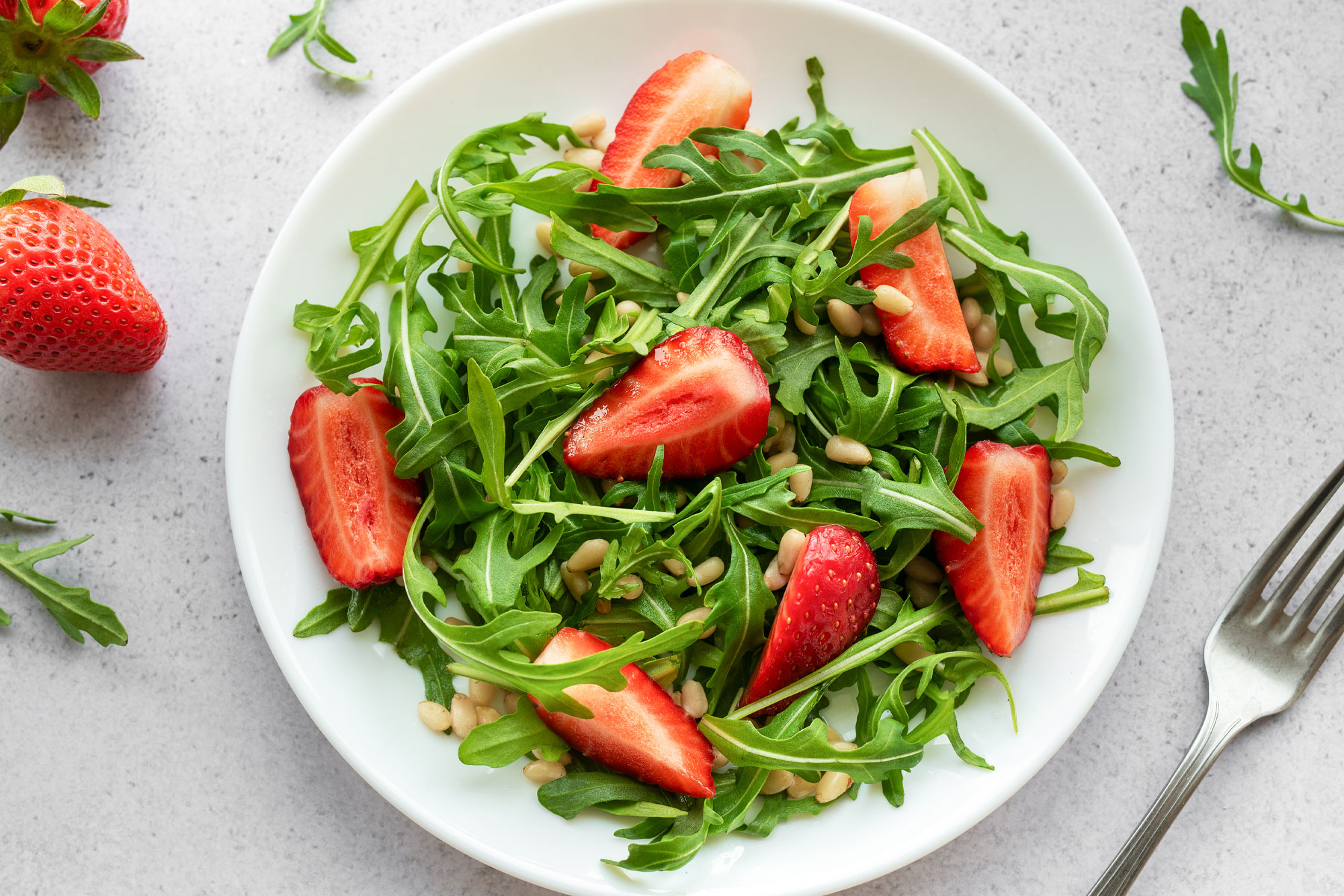 Teller mit grünem Rucolasalat und frischen Erdbeeren, angerichtet mit Dressing