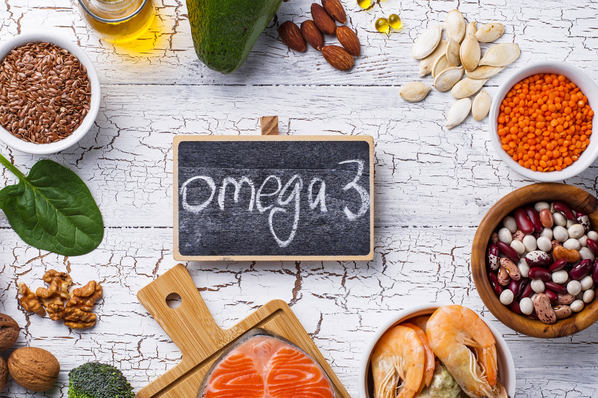 Verschiedene Lebensmittel wie Nüsse, Lachs, Samen und Öle um eine Tafel mit Schriftzug „Omega 3“
