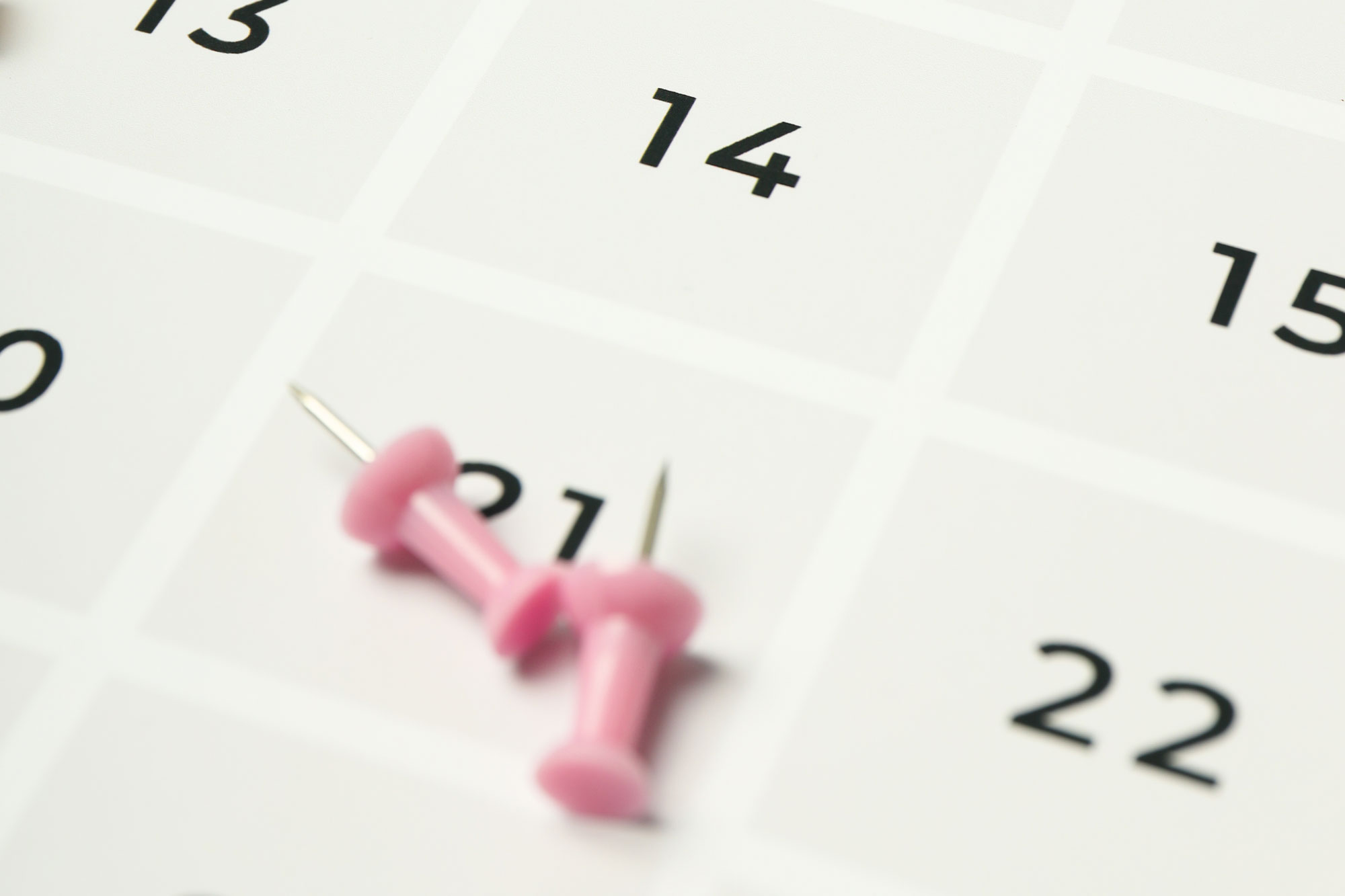 Nahaufnahme eines Kalenders mit eingestecktem rosa Pin bei einem Datum