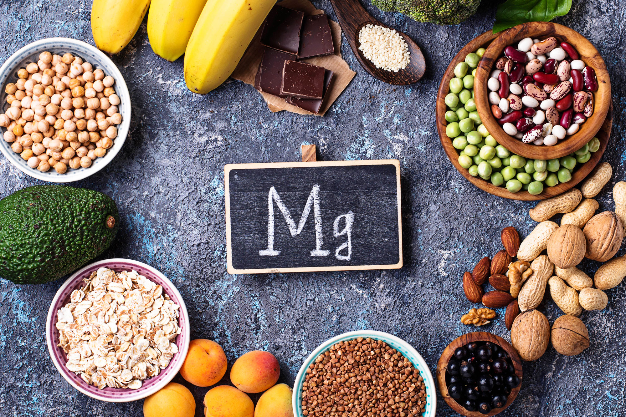 Lebensmittel wie Nüsse, Samen, Bananen und Gemüse rund um eine Tafel mit der Aufschrift „Mg“