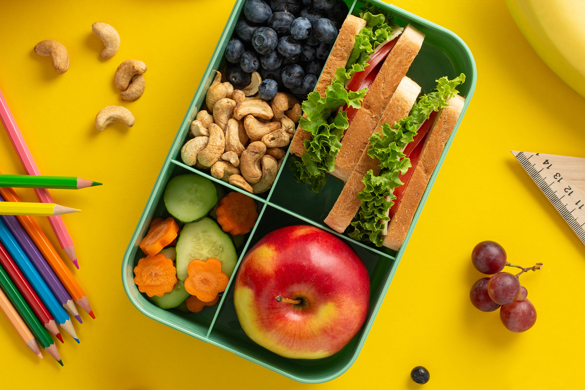 Bunte Brotdose mit Obst, Gemüse und Snacks auf gelbem Hintergrund
