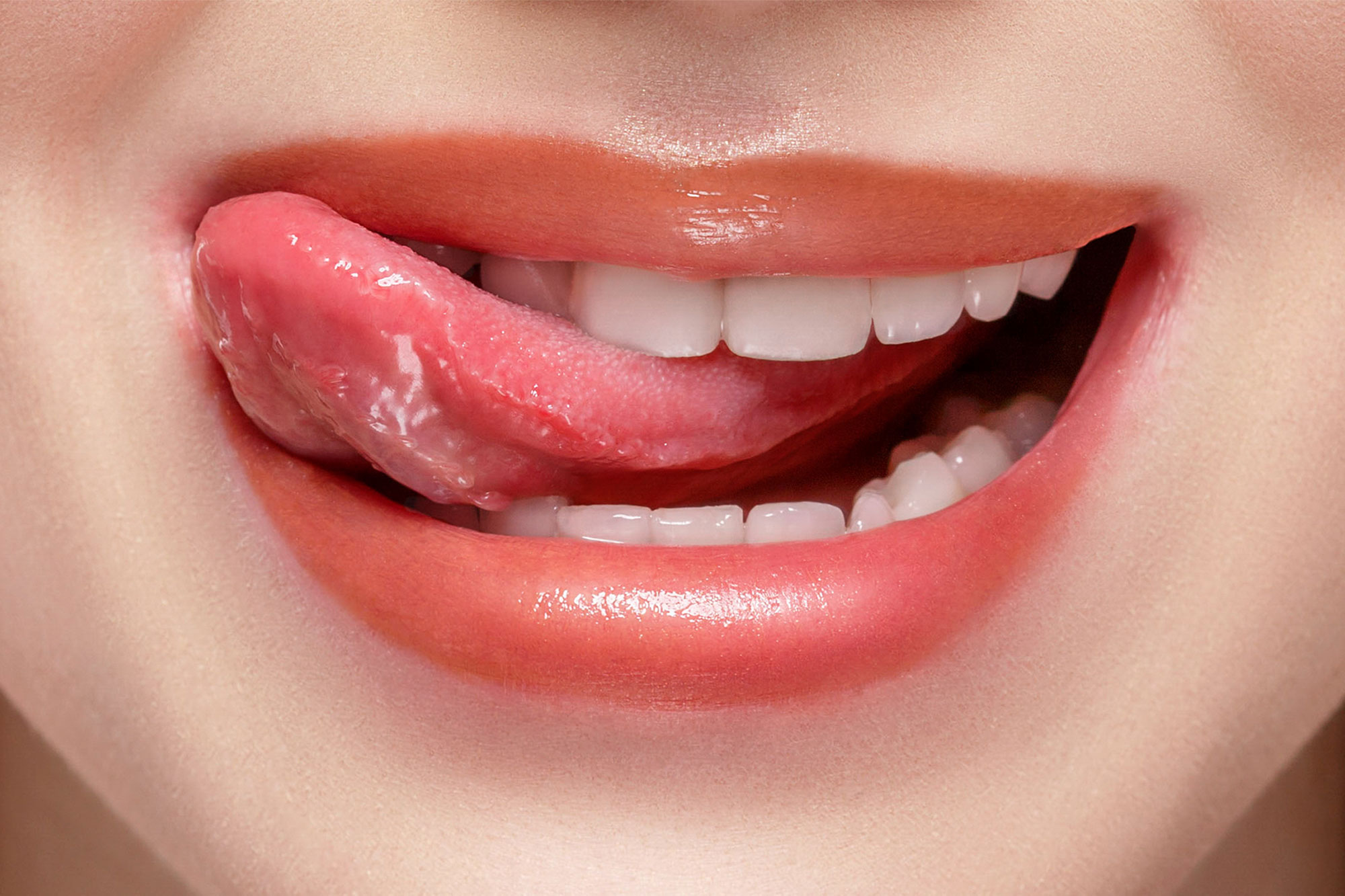 Frau lächelt und fährt mit der Zunge spielerisch über ihre weißen Zähne