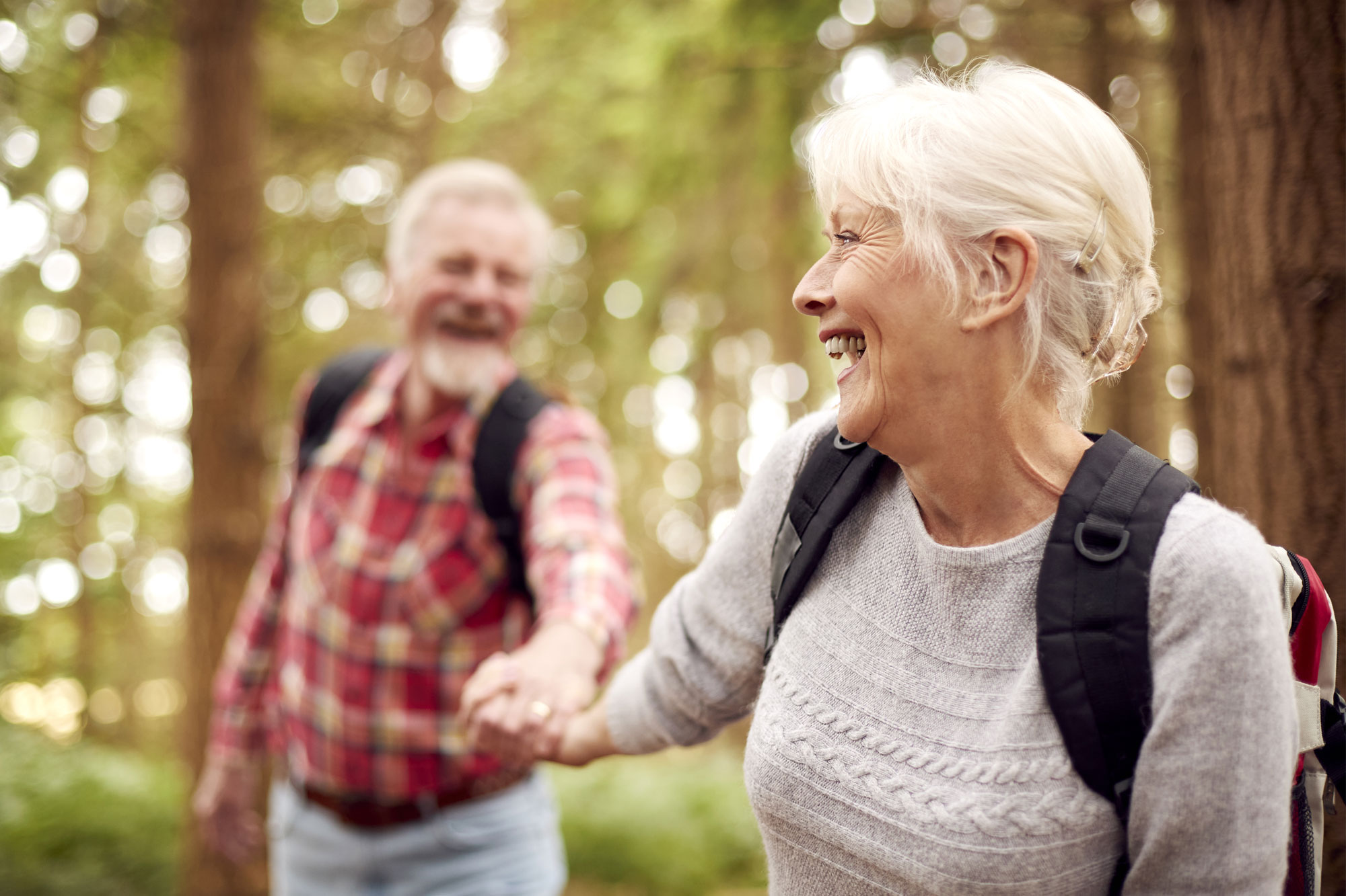Zwei ältere Personen lachen im Wald und halten sich an den Händen.