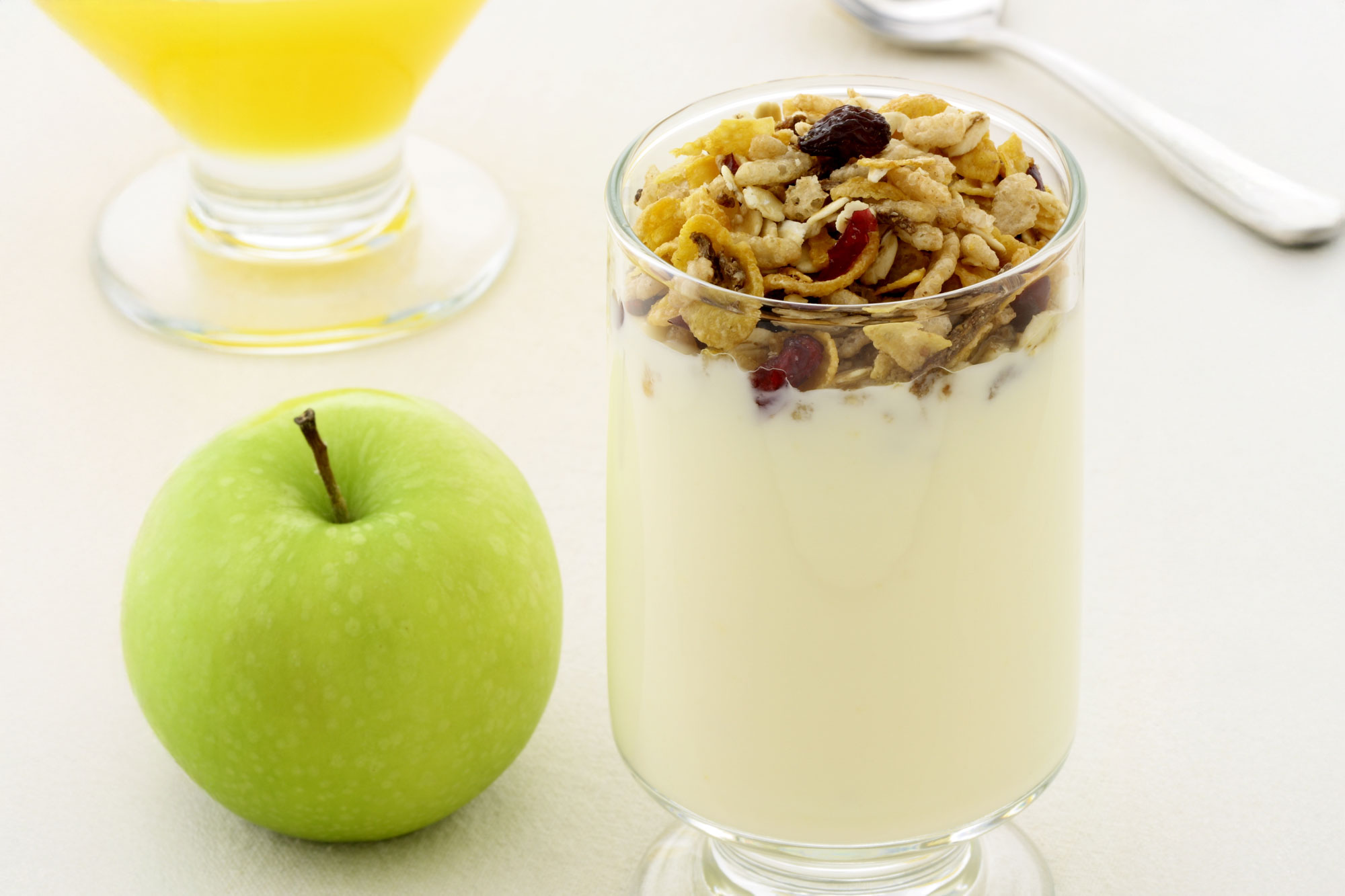 Glas mit cremigem Joghurt und Topping, daneben grüner Apfel