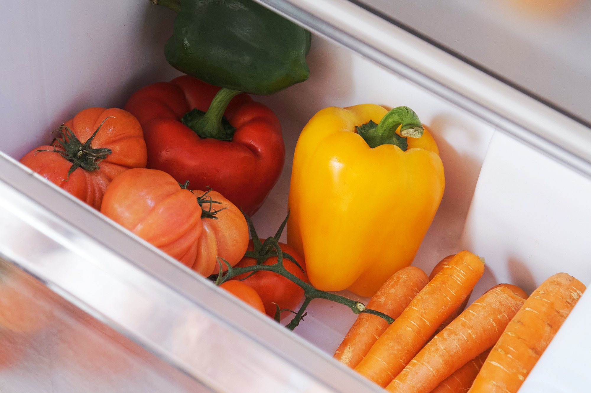 Paprika, Karotten und weiteres Gemüse im geöffneten Kühlschrankfach.