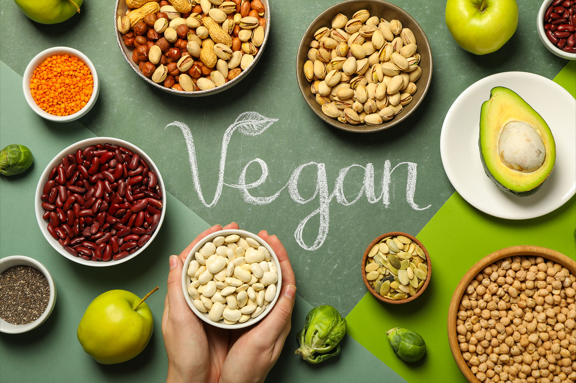 Verschiedene pflanzliche Lebensmittel um das Wort „Vegan“ auf grünem Hintergrund angeordnet